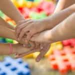 Seven children’s hands coming together in unison.