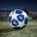 A static blue and white UEFA league branded Adidas football on the turf, under floodlights.