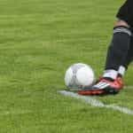 A footballer kicking a ball on a grass pitch.