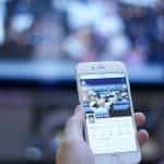 A person holding up a smartphone in front of a television screen.