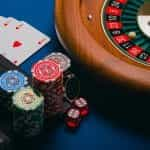 Roulette wheel, casino chips and cards placed next to a laptop.