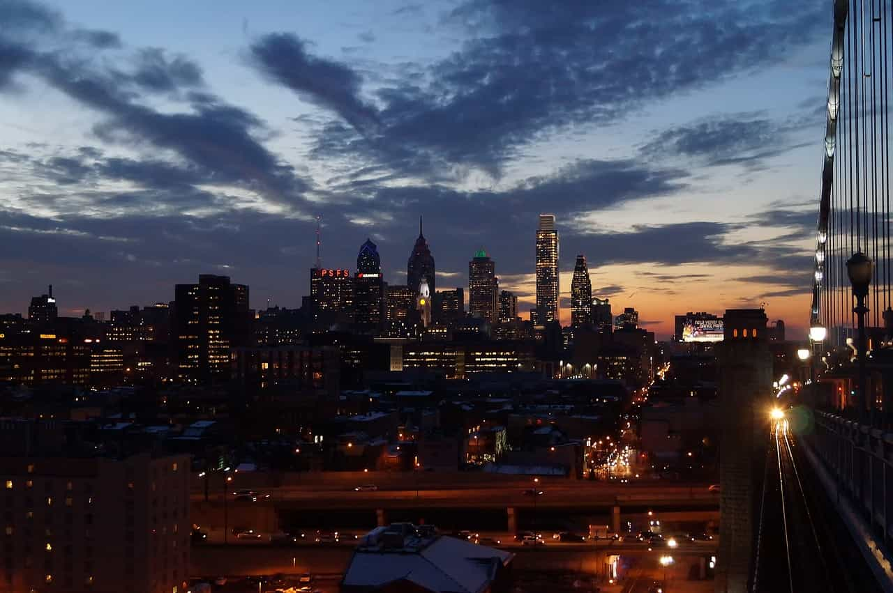 The skyline of downtown Philadelphia, Pennsylvania from the side of a bridge leading away from the city, with many tall skyscrapers and buildings making up the city’s center area.