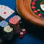 A roulette wheel, playing cards, poker chips and dice with a laptop.