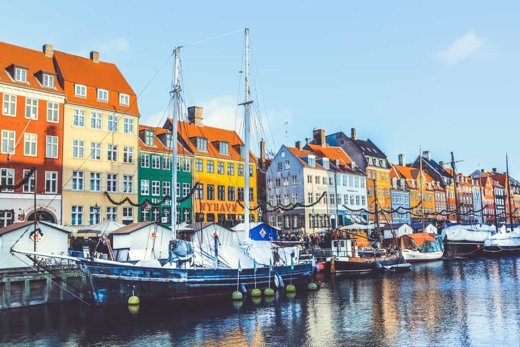 Sail boats docked in a river in front of buildings.