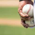 A pitcher at a baseball game holding two baseballs in his left hand as he prepares to throw one at the batter.